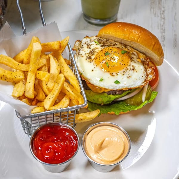 A Cosmo Eatery burger with a fried egg, lettuce, tomato, and onion, served with fries and sauces.