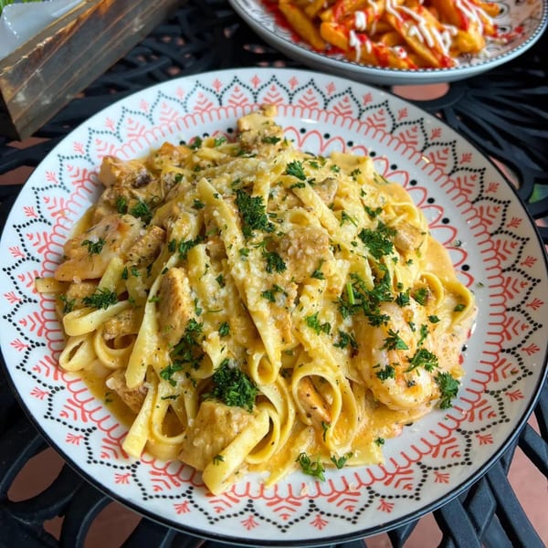 Creamy fettuccine pasta with chicken, shrimp, and parsley on a decorative plate, with fries in the background.