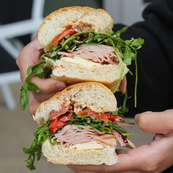 Hands holding a large Cosmo Eatery sandwich, filled with turkey, cheese, arugula, and tomatoes.